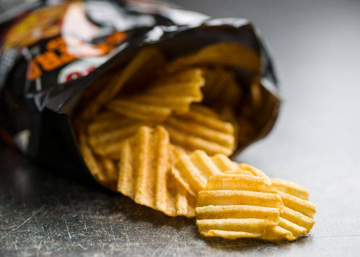 An open bag of crinkle-cut chips, with a few chips spilling out of the bag.